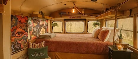A cozy interior with a bed, a pillow with 'love' text, a small table with a candle, and a mural on the wall.