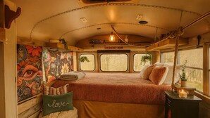 Un interior acogedor con una cama, un almohadón con la palabra 'love', una mesita con una vela y un mural en la pared.