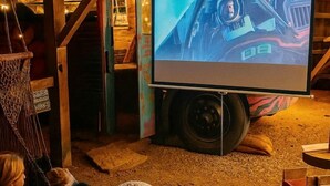Una pantalla proyecta un vehículo, una hamaca y una escalera en un entorno rústico.