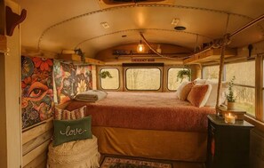 Ein gemütliches Interieur mit einem Bett, einem Kissen mit dem Schriftzug 'love', einem kleinen Tisch mit einer Kerze und einem Wandgemälde.