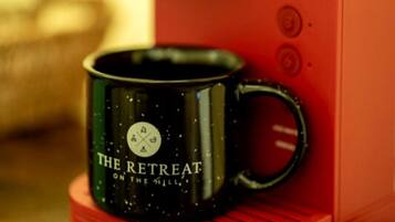 Punainen kahvinkeitin ja musta kahvimuki, jossa on teksti ”THE RETREAT ON THE MILE”.