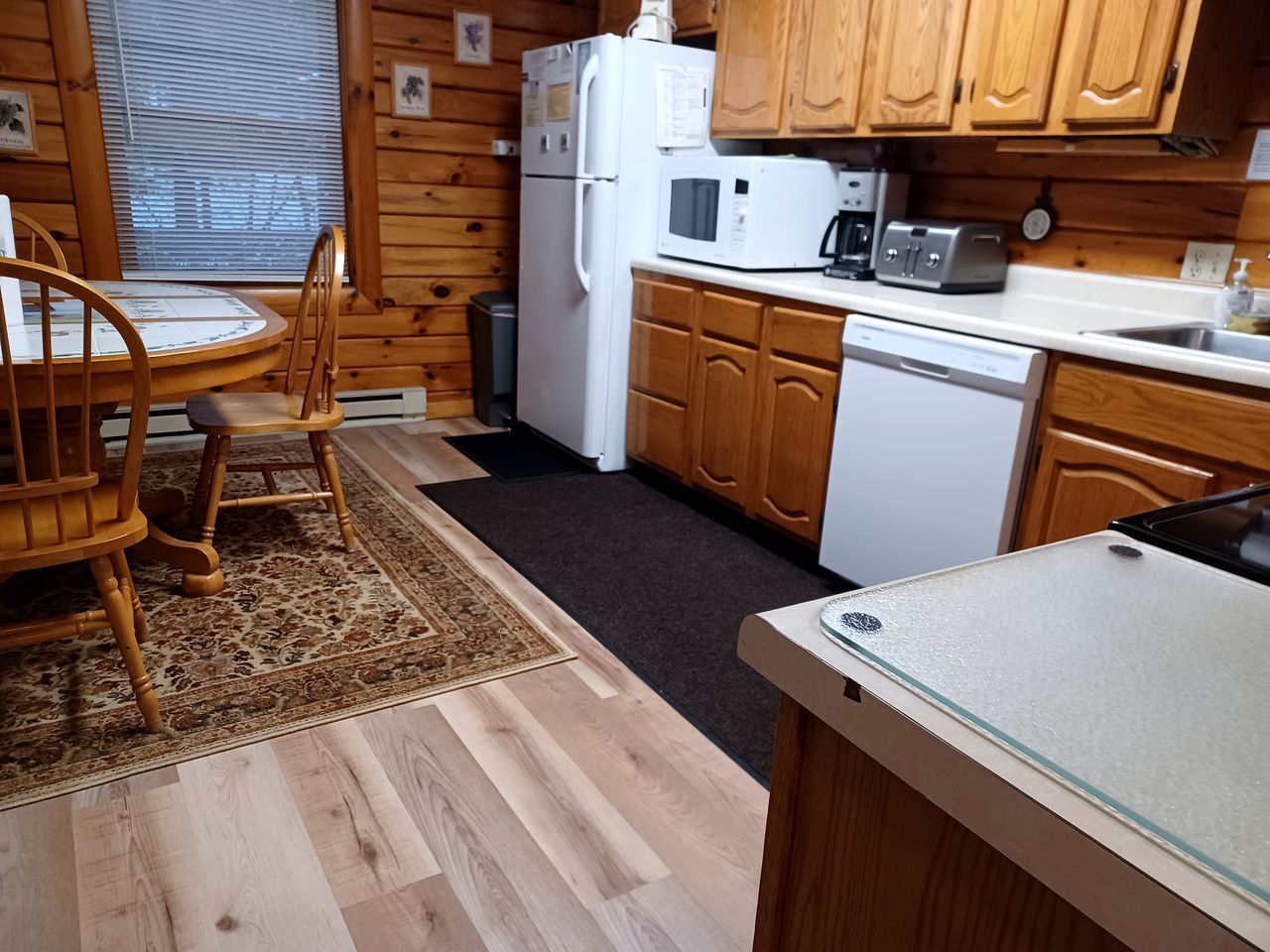A compact kitchen with wooden cabinets, a refrigerator, a microwave, a toaster, and a dishwasher.