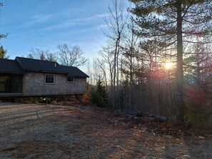 A house with a sloped roof, a front porch, and a yard with trees and a gravel path.