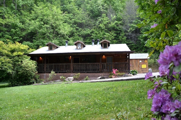 A wooden cabin with a porch, surrounded by lush greenery and a well-maintained lawn. - Rustic Family-Friendly Log Cabin in the Smoky Mountains, North Carolina (Cherokee)