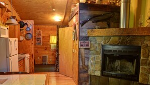A cozy cabin interior with a stone fireplace, wooden walls, a dining area, and a kitchen with a refrigerator and stove. - Rustic Family-Friendly Log Cabin in the Smoky Mountains, North Carolina (Cherokee)
