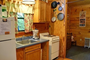 A compact kitchen with wooden cabinets, a stove, a coffee maker, and a sink. - Rustic Family-Friendly Log Cabin in the Smoky Mountains, North Carolina (Cherokee)