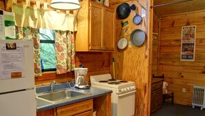 A compact kitchen with wooden cabinets, a stove, a coffee maker, and a sink. - Rustic Family-Friendly Log Cabin in the Smoky Mountains, North Carolina (Cherokee)