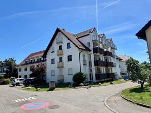 Um edifício residencial de vários andares com varandas, céu claro e uma placa 'ZONEN' na rua.