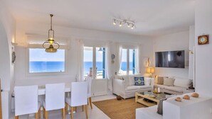 Ein helles Interieur mit Essbereich, Sofas, einem Fernseher und Blick auf das Meer.