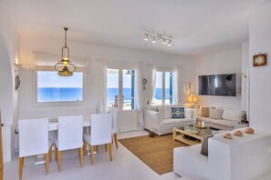 Ein helles Interieur mit Essbereich, Sofas, einem Fernseher und Blick auf das Meer.
