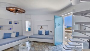 Ein Zimmer mit Steinboden, einer blauen Tür, einem weißen Sofa und einem Glastisch.