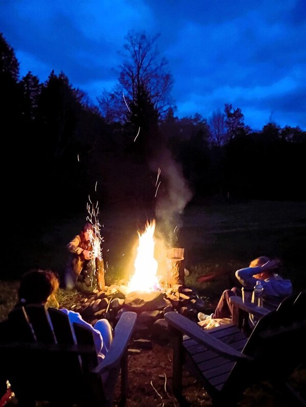 A campfire with people sitting on chairs around it.