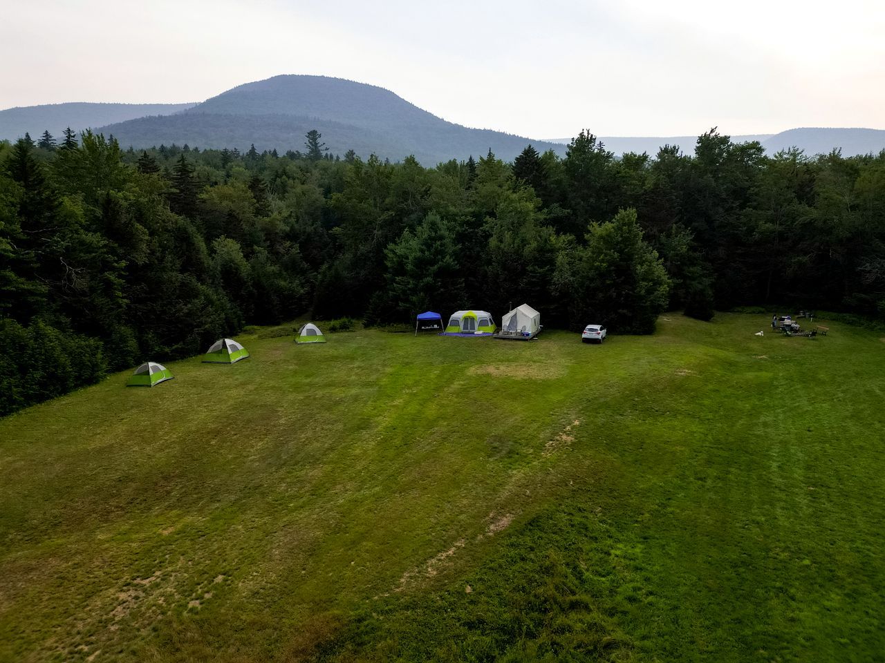 En campingplats med tält och en bil, omgiven av träd och med ett berg i bakgrunden.