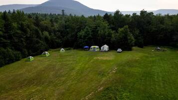 En campingplats med tält och en bil, omgiven av träd och med ett berg i bakgrunden.
