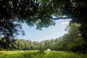 Paesaggio rurale con un edificio bianco immerso nel verde e colline sullo sfondo.