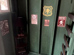 A room with a green door, a poster of a person, and a sign indicating a bigfoot breeding area. - Scenic Off-Grid Campsite Overlooking Crystal Clear Lake in Sagle, Idaho (Sagle)