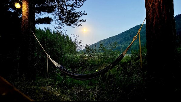 A hammock between trees with a view of a forested hill and a distant town.