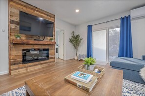 Una sala de estar con una estantería de madera, un televisor de pantalla plana, una chimenea, un sofá y una mesa de centro con libros.