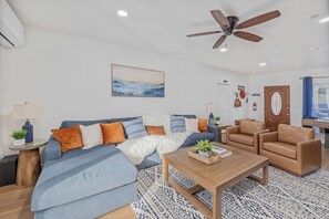 Ein Wohnzimmer mit einer Couch, Sesseln, einem Couchtisch, einem Deckenventilator und einem Gemälde an der Wand.