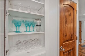 Een opslagruimte met schappen vol verschillende glazen, waaronder drinkglazen voor buiten en wijnglazen.