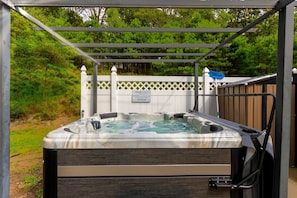 A hot tub under a pergola with a white fence and a sign in the background.