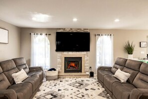 A living room with two sofas, a fireplace, and a flat-screen TV. - Modern Villa with Sauna, Pool & Panoramic Views in Bushkill, Pennsylvania (Bushkill)