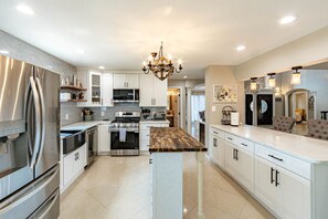 A modern kitchen with stainless steel appliances, white cabinetry, and a central island with a wooden countertop.