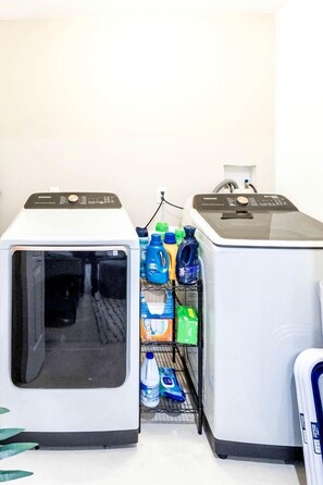 A laundry room with two washing machines and a shelf with various laundry detergents. - Modern Villa with Sauna, Pool & Panoramic Views in Bushkill, Pennsylvania (Bushkill)