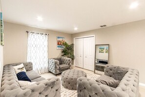 A living room with a grey sofa set, a grey armchair, a white door, and a plant. - Modern Villa with Sauna, Pool & Panoramic Views in Bushkill, Pennsylvania (Bushkill)