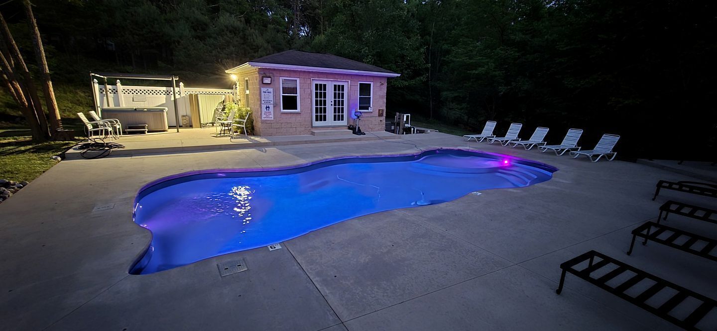 Une piscine avec des chaises longues et un petit bâtiment doté d’une porte et de fenêtres.