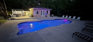 A swimming pool with lounge chairs and a small building with a door and windows.