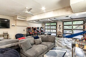 A living room with a sofa, a foosball table, arcade games, and a large window.