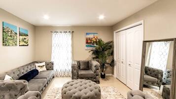 Un salon comprenant un canapé, un pouf et un fauteuil, une grande plante en pot et une porte dotée d’un miroir.