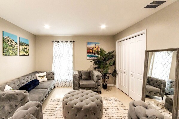 A living room with a sofa, ottoman, and armchair, a large potted plant, and a door with a mirror. - Modern Villa with Sauna, Pool & Panoramic Views in Bushkill, Pennsylvania (Bushkill)