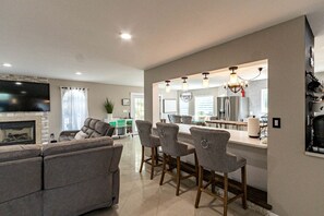 A modern living room with a fireplace, a dining area with bar stools, and a kitchen with a large island. - Modern Villa with Sauna, Pool & Panoramic Views in Bushkill, Pennsylvania (Bushkill)