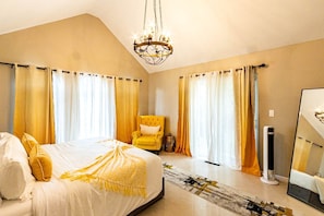 A bedroom with a bed, a chair, a mirror, and a chandelier.