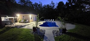 A backyard with a swimming pool, lounge chairs, and a patio area.