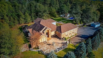 Een luchtbeeld van een groot, meerlaags huis met een gevel van natuursteen, een ruime oprit en een verzorgd gazon.