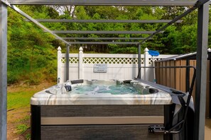A hot tub under a pergola with a white fence and a sign in the background. - Modern Villa with Sauna, Pool & Panoramic Views in Bushkill, Pennsylvania (Bushkill)
