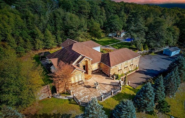 An aerial view of a large, multi-story house with a stone facade, a spacious driveway, and a well-maintained lawn.