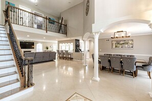 A spacious living area with a staircase, a dining area with chairs, and a kitchen in the background.
