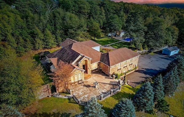 An aerial view of a large, multi-story house with a stone facade, a spacious driveway, and a well-maintained lawn.