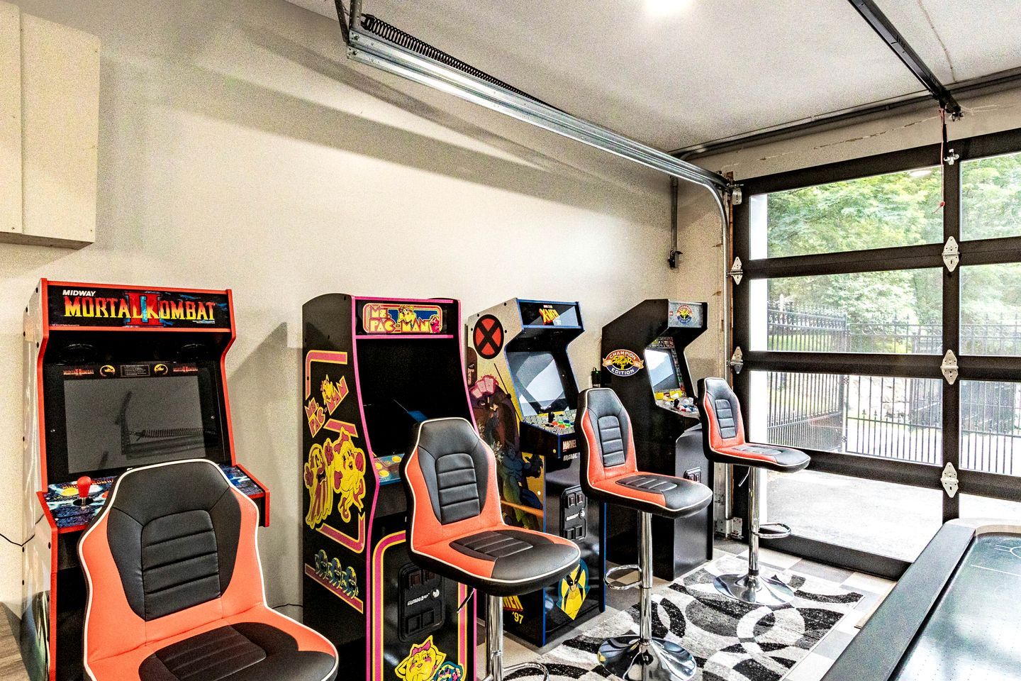 Une rangée de bornes d’arcade avec des sièges, un sol carrelé et une porte de garage avec des fenêtres.