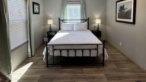 Een slaapkamer met een bed, twee nachtkastjes, een raam met gordijnen, een foto aan de muur en een plafondlamp.