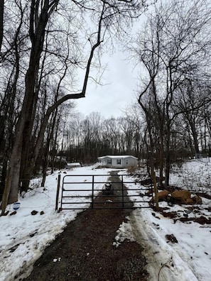 A snow-covered path leading to a white mobile home in a wooded area. - Peaceful Farmstead Cottage with Creekside Views Near Iron Station, North Carolina (Iron Station)