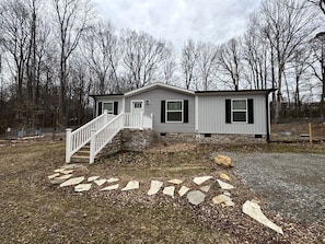 A two-story house with a stone pathway leading to the front door, surrounded by a wooded area. - Peaceful Farmstead Cottage with Creekside Views Near Iron Station, North Carolina (Iron Station)