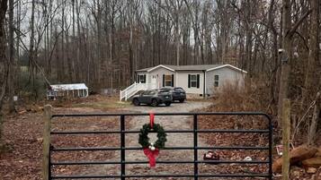 A gated entrance with a wreath, a house in the background, and a forested area.