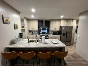 Una cocina moderna con una isla central, taburetes de bar y un refrigerador de acero inoxidable.