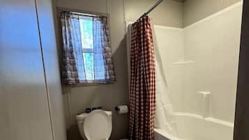 A compact bathroom with a toilet, a shower, and a window with curtains.