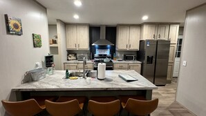 Een moderne keuken met een centraal eiland, barkrukken en een roestvrijstalen koelkast.